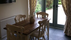 A dining area with a wooden table and four chairs, a vase with flowers, and a television on the wall. - Romantic Rural Retreat, Ideal Base to Explore Cornwall (Wadebridge)