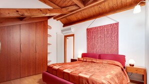 Een slaapkamer met een houten plafond, een groot bed met een rode hoofdbord, een kledingkast en een radiator.
