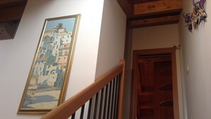 Een trap met een houten leuning en een lijst met een schilderij van een kustplaats op de muur.