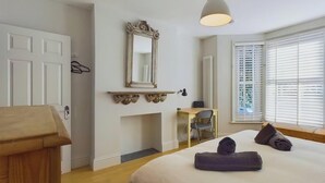 A bedroom with a bed, a desk, a chair, a mirror, and a window with blinds. - Blackberry Cottage, Bembridge | Accessible Coastal (Bembridge)