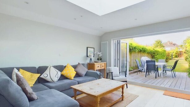 A modern living room with a grey sofa, a wooden coffee table, and a sliding glass door leading to an outdoor patio with a table and chairs. - Blackberry Cottage, Bembridge | Accessible Coastal (Bembridge)