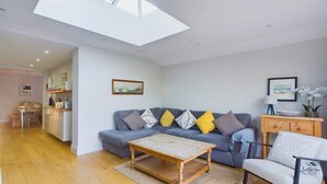 A modern living room with a sofa, a coffee table, and a dining area with a chair and table. - Blackberry Cottage, Bembridge | Accessible Coastal (Bembridge)