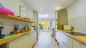 A narrow kitchen with wooden countertops, a coffee machine, and a view to the outside. - Blackberry Cottage, Bembridge | Accessible Coastal (Bembridge)