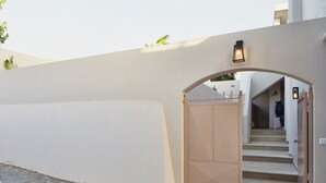 Un mur extérieur de couleur beige, avec un portail en bois et un escalier menant à une entrée abritée.