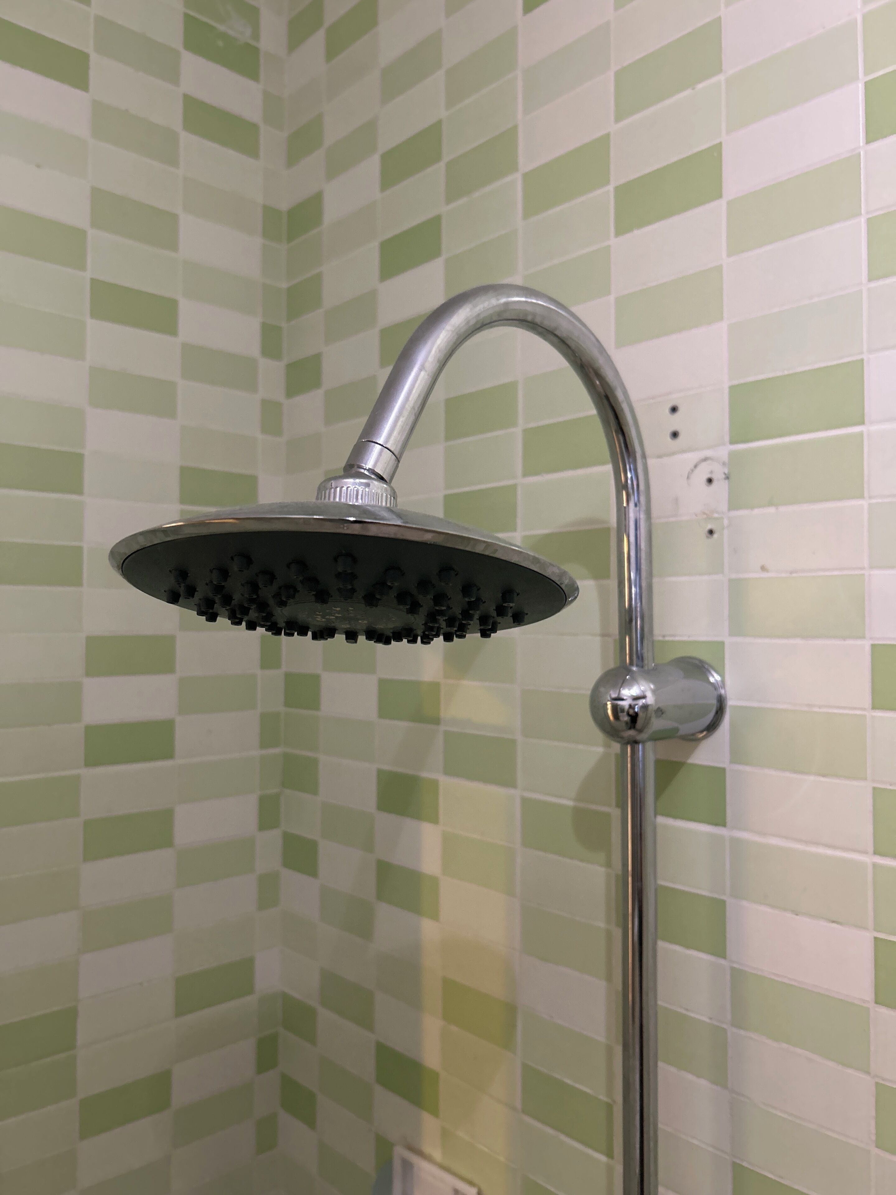 A showerhead with a curved arm and a round base, mounted on a wall with green and white checkered tiles.