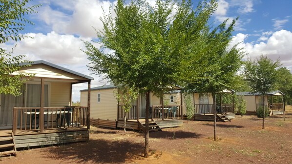 A row of mobile homes with wooden decks and a tree in the foreground.