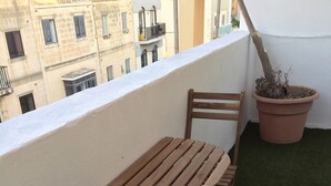 Un balcón con una mesa y sillas de madera, una planta en maceta y vistas de edificios al fondo.
