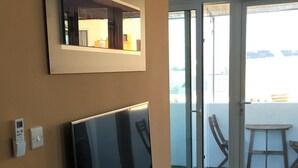 Ein modernes Wohnzimmer mit einem an der Wand montierten Flachbildfernseher, einem weißen Konsolentisch mit Dekoration und einer Schiebetür zu einem Außenbereich mit Tisch und Stühlen.