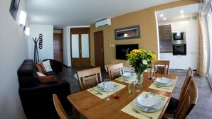 Un área de comedor con una mesa de madera dispuesta para cuatro personas, un sofá y un televisor montado en la pared.