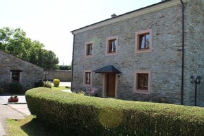 Un bâtiment en pierre avec une entrée centrale, de nombreuses fenêtres et une haie bien entretenue.