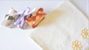 Un paño blanco con estampado floral y una caja de regalo con cintas.