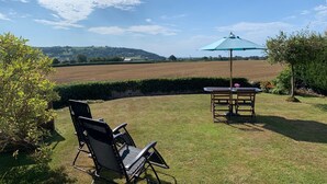 A patio with a table and chairs, a table umbrella, and a view of a field and hills.