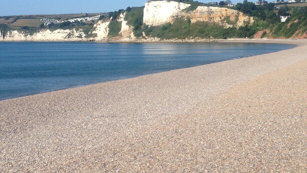 A pebble beach with a white cliff and a clear blue sky.