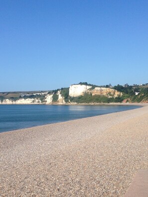 Une plage de galets bordée d’une falaise blanche et surplombée d’un ciel bleu azur.