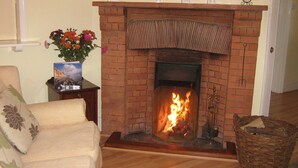 A living room with a brick fireplace, a sofa, a side table with a vase of flowers, and a basket.
