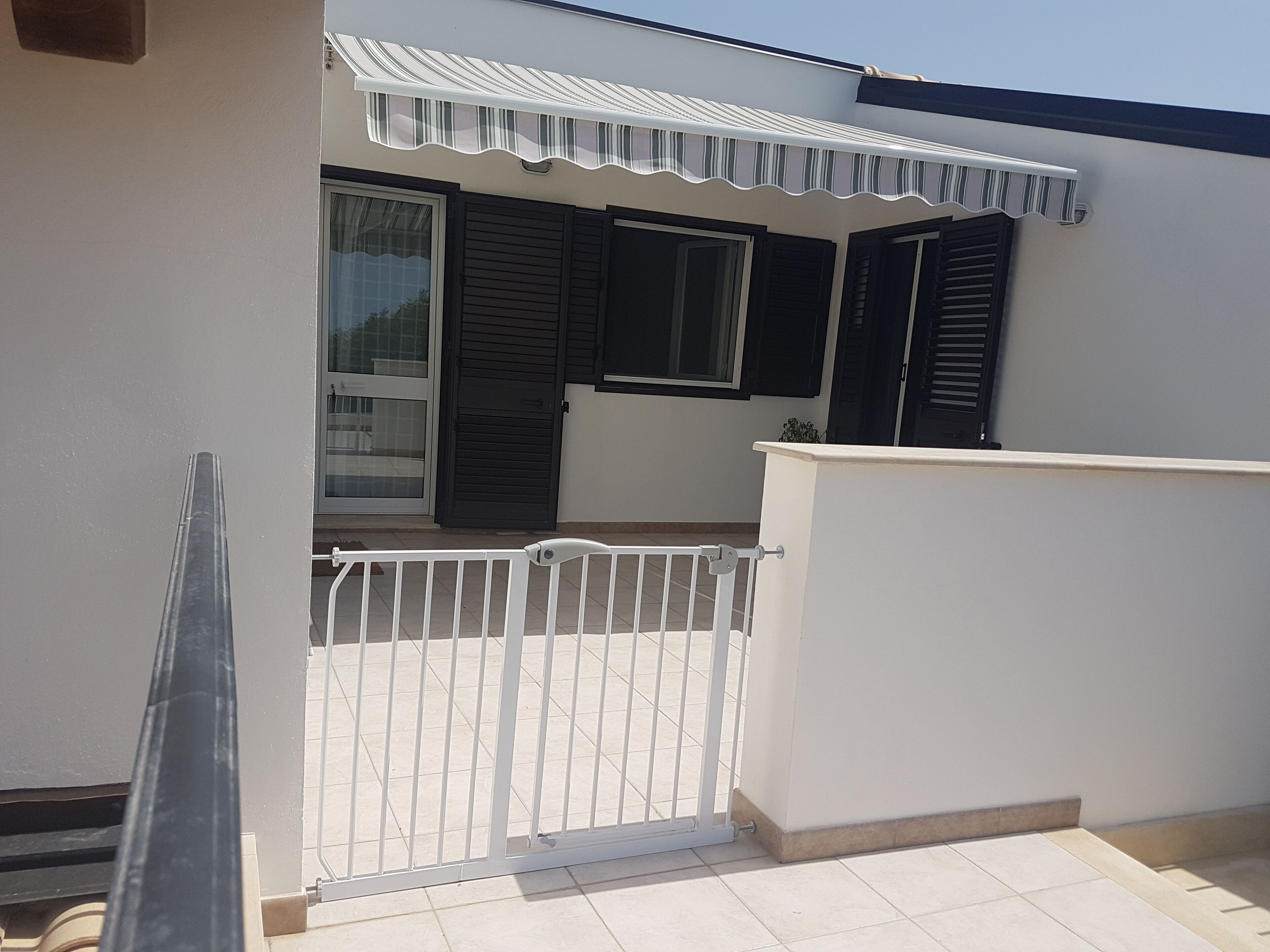 A residential building with a white exterior, a balcony with a white railing, and a gated entrance.
