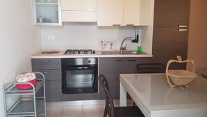 Cocina compacta con estufa a gas, horno, armarios blancos y una pequeña mesa de comedor con sillas.
