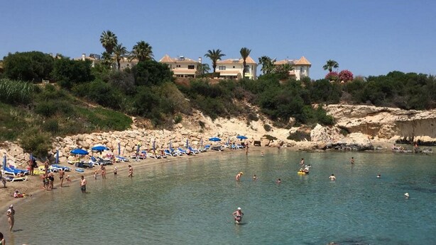 A beach with clear water, umbrellas, and people swimming.