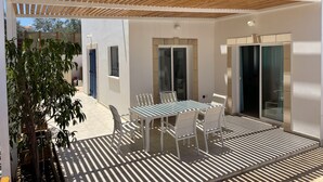 A covered outdoor patio with a table and chairs, a pergola, and a view of the street.