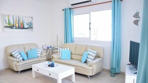 A modern living room with two beige sofas, a white coffee table, and a TV on a stand.