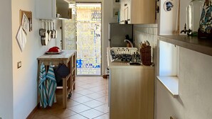 Kompakti keittiö, jossa on keskeinen saareke, ruokailutila pöytineen ja tuoleineen sekä näkymä lasiovesta parvekkeelle.