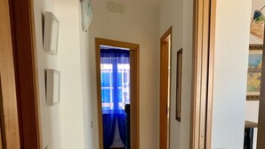 Käytävässä on sinivalkoraidallinen matto, puiset ovet ja näkymä huoneeseen, jossa on ikkuna ja verhot.