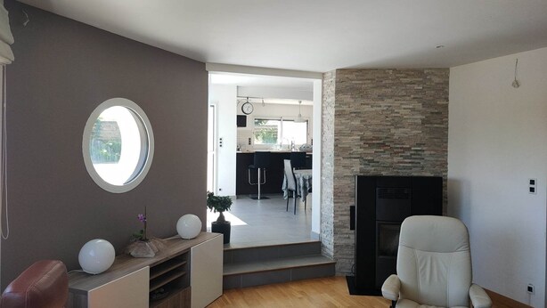 A modern living room with a fireplace, a round window, and a view into the kitchen area. - superb house ideally located 220 m2 (Sainte-Sève)