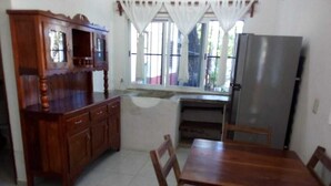 Una cocina con una mesa de madera, sillas, un refrigerador y un armario.