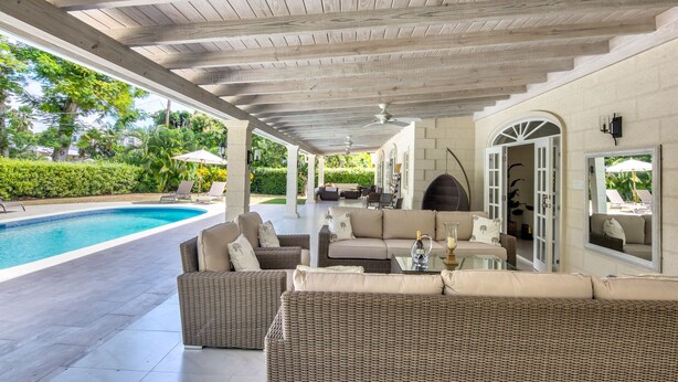 Une terrasse extérieure avec une piscine, des meubles en osier et un toit abrité.