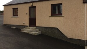 A single-story building with a beige exterior, a dark brown door, and two windows with dark frames. - 1 Bedroom Chalet 30 Minute Walk From Stornoway Town Centre (Stornoway Isle of Lewis)
