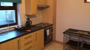 A compact kitchen with wooden cabinets, a gas stove, and a stainless steel sink. - 1 Bedroom Chalet 30 Minute Walk From Stornoway Town Centre (Stornoway Isle of Lewis)