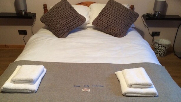 A neatly made bed with two pillows, a folded towel on each side, and a sign indicating 'Lewis Self Catering'. - 1 Bedroom Chalet 30 Minute Walk From Stornoway Town Centre (Stornoway Isle of Lewis)