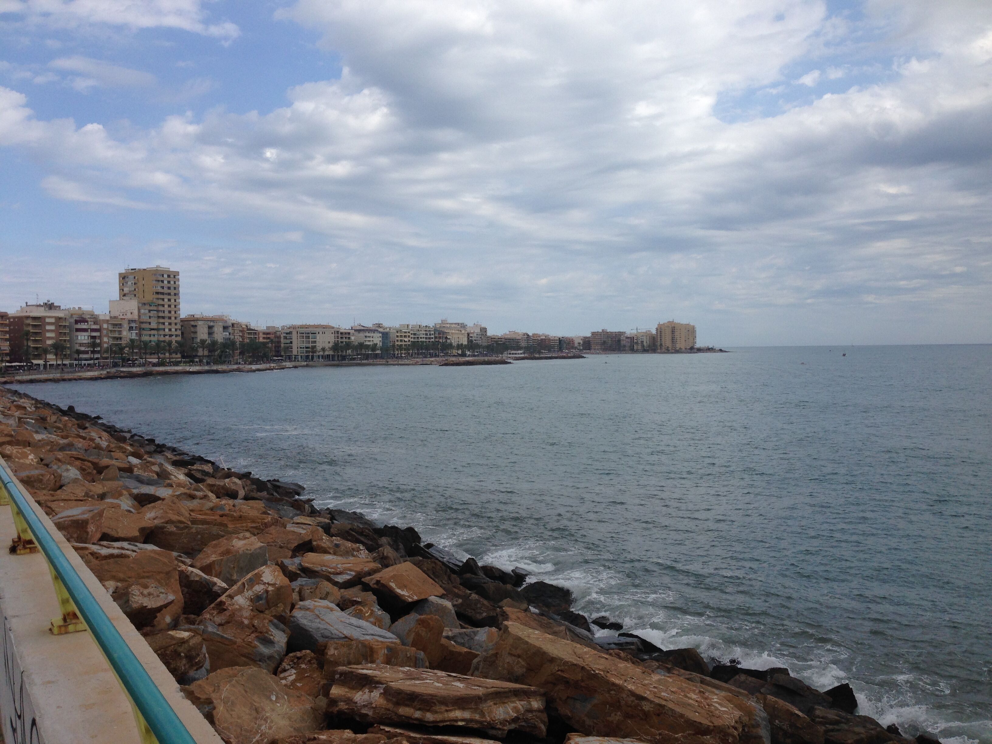 A coastal cityscape with a rocky shoreline, buildings, and a clear sky.