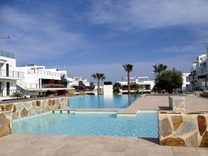 A modern hotel with a central swimming pool, stone-tiled poolside, and palm trees.