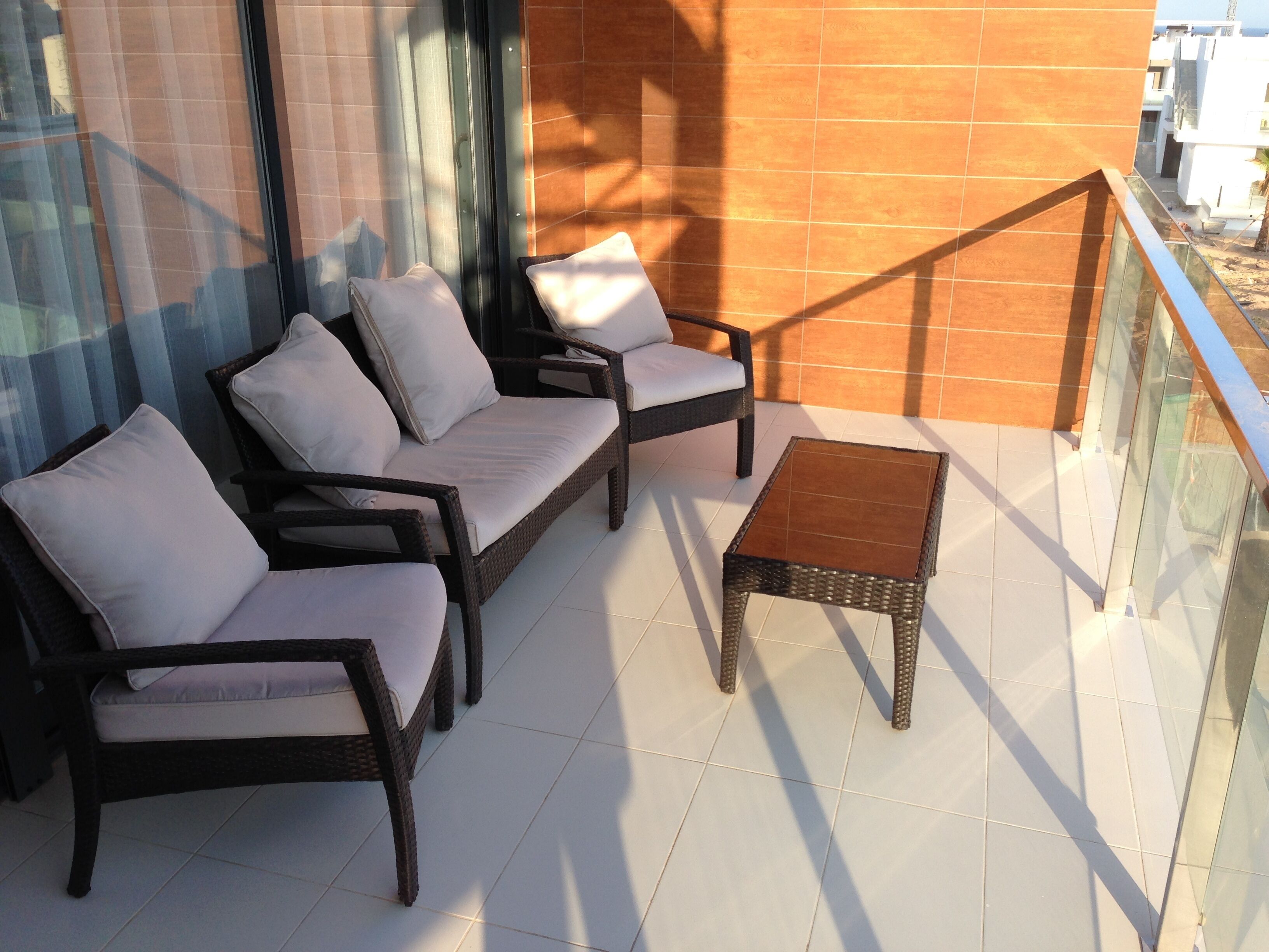 Een balkon met rieten meubilair, waaronder een bank en een kleine tafel, met uitzicht op gebouwen op de achtergrond.