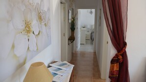 A hallway with a painting of white flowers, a lamp, and a table with books.