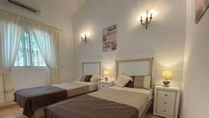 A hotel room with two beds, a window with curtains, a wall-mounted picture, and a nightstand with a lamp.