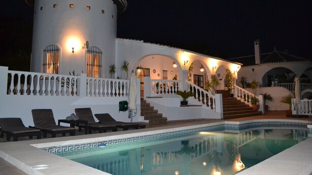 A luxurious poolside area with a large pool, a white building with arches, and a staircase leading to a balcony.