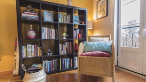 Ein Zimmer mit Bücherregal, Korbsessel mit Kissen und einem Korb auf dem Boden.