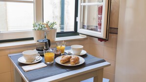 Ein Frühstückstisch mit Croissants, Orangensaft und Kaffee, neben einem Fenster mit Blumentöpfen.