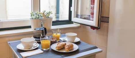A breakfast table with croissants, orange juice, and coffee, set by a window with potted plants.