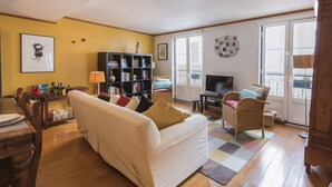 Ein Wohnzimmer mit einer Couch, einem Bücherregal, einem Fernseher und einem Essbereich mit Stühlen und einem Tisch.