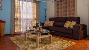 A living room with a brown sofa, glass coffee table, and sheer curtains. - Wonderful View Apartment with Fantastic sunsets (Florenças, Arco da Calheta)