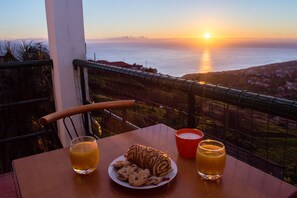 A table with a plate of cookies and two glasses of orange juice, a candle, and a view of the sunset over the ocean. - Wonderful View Apartment with Fantastic sunsets (Florenças, Arco da Calheta)