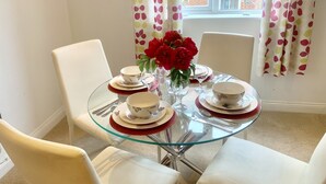 Una mesa de comedor con cuatro sillas blancas, cubierta de cristal y un florero con flores rojas.