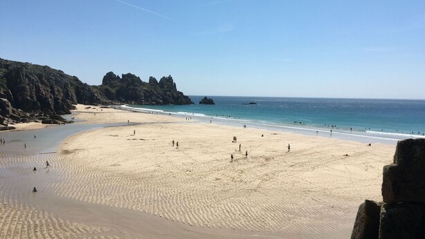 Una extensa playa de arena con acantilados rocosos a un lado y un cielo azul despejado.