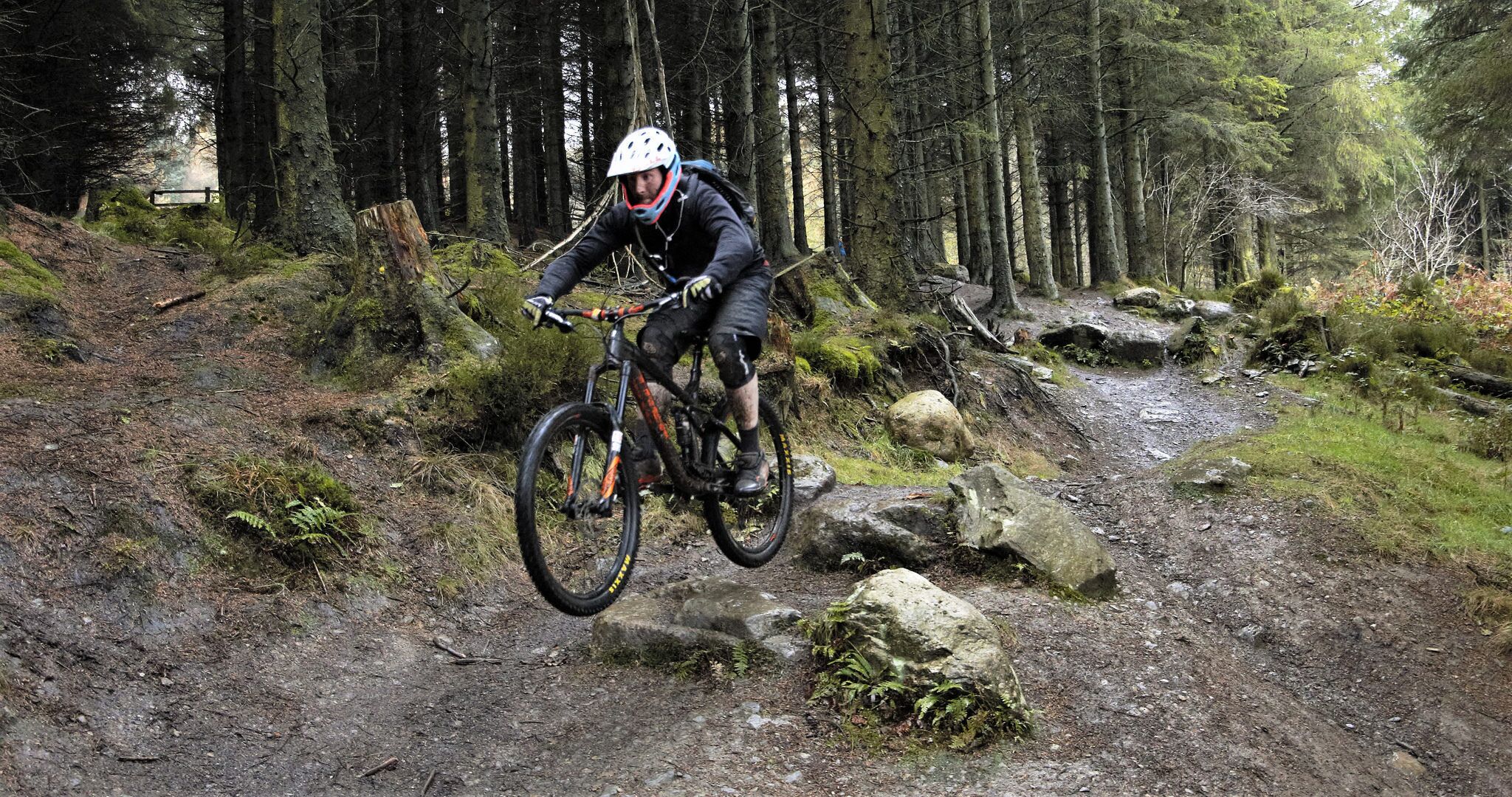A mountain biker navigating a rocky trail in a forested area.