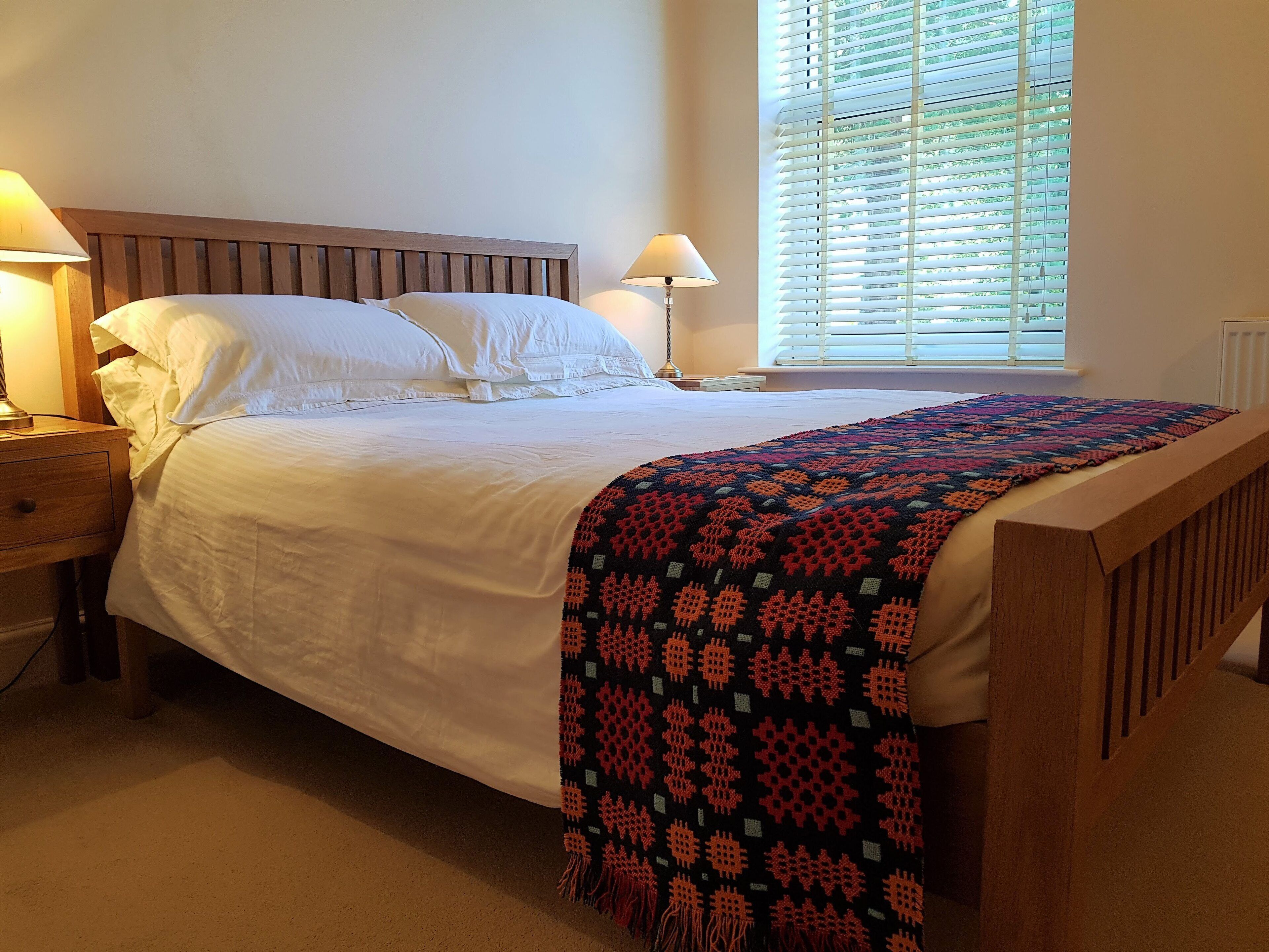 A neatly made bed with white linens, a wooden headboard, and a colorful blanket.