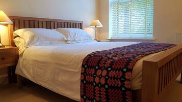 A neatly made bed with white linens, a wooden headboard, and a colorful blanket.
