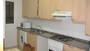 A compact kitchen with a microwave, sink, stove, and washing machine. - Apartment Fira HUTB-014228 (L'Hospitalet de Llobregat)